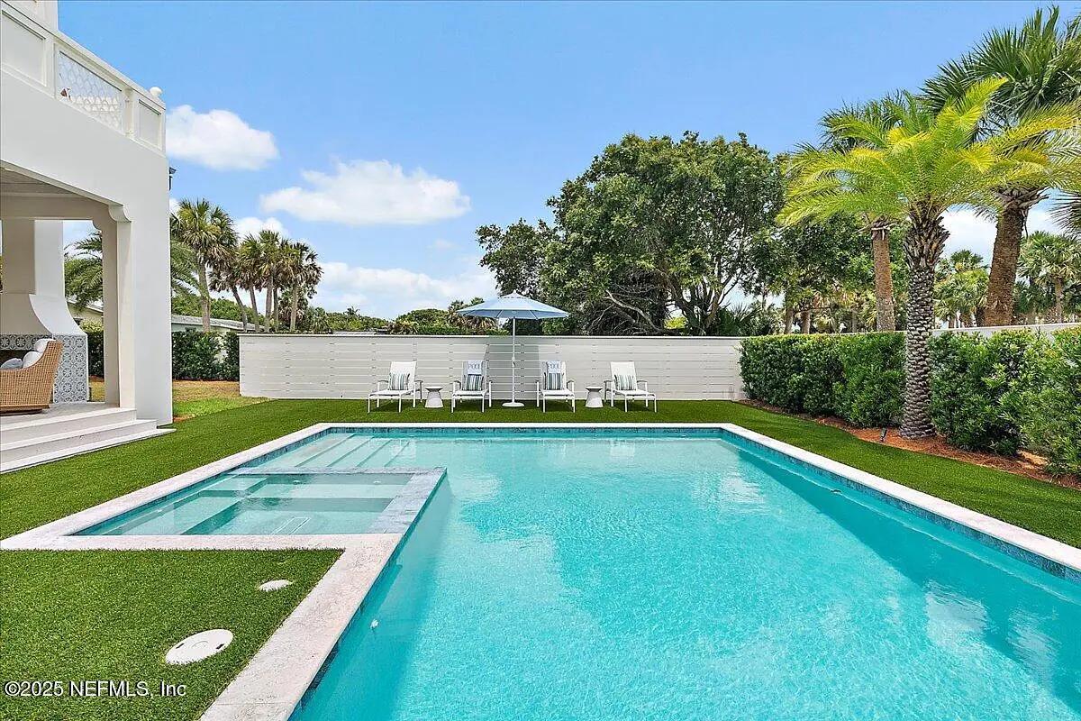 Exterior rear space with swimming pool, marble decking, lounge chairs, umbrella, and palm trees