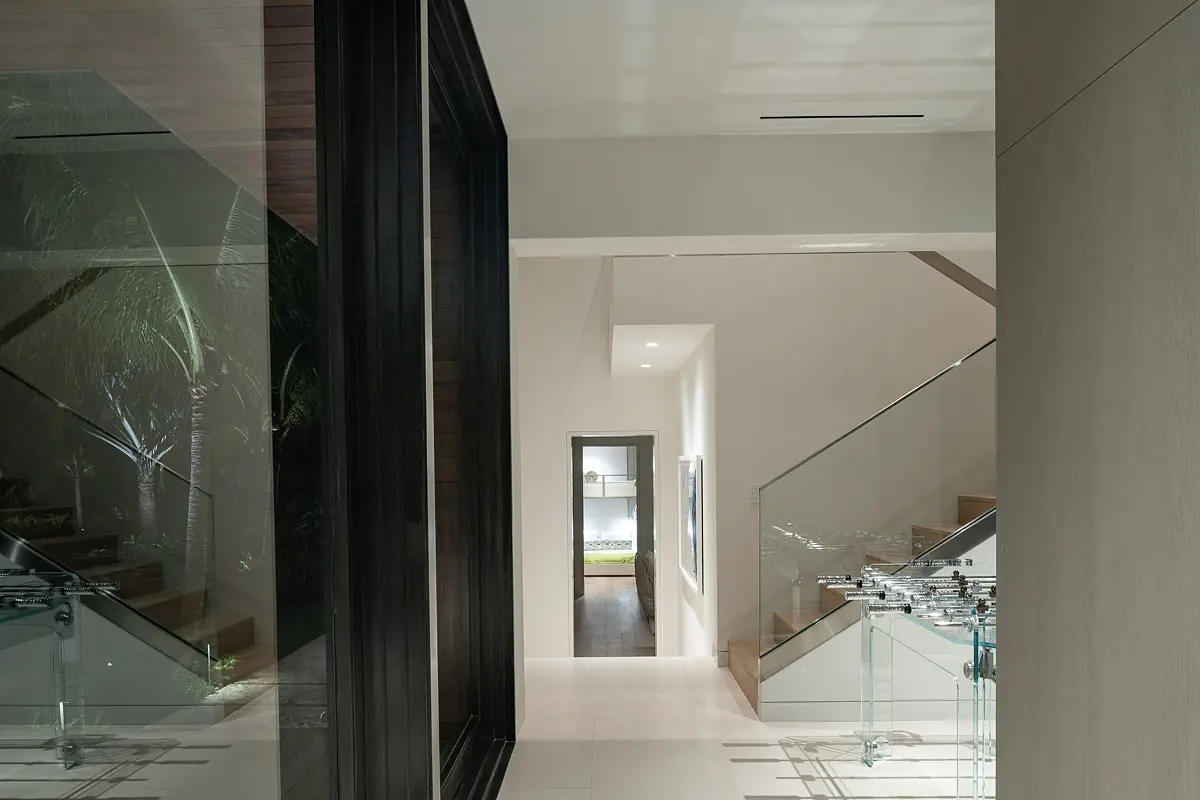 Hallway with glass railing staircase, doorframe, large glass wall, and tiled floor.