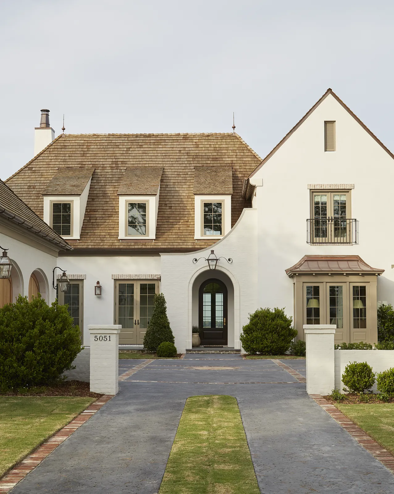 Front exterior view of a house with sloped roof, white walls, archway, and paved driveway