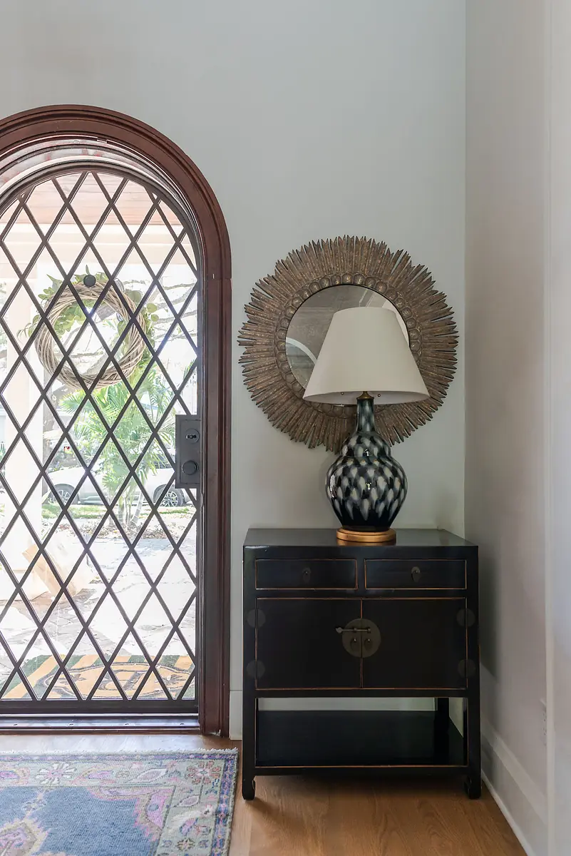 Foyer with side table, black and white vase, sunburst mirror, and patterned area rug.