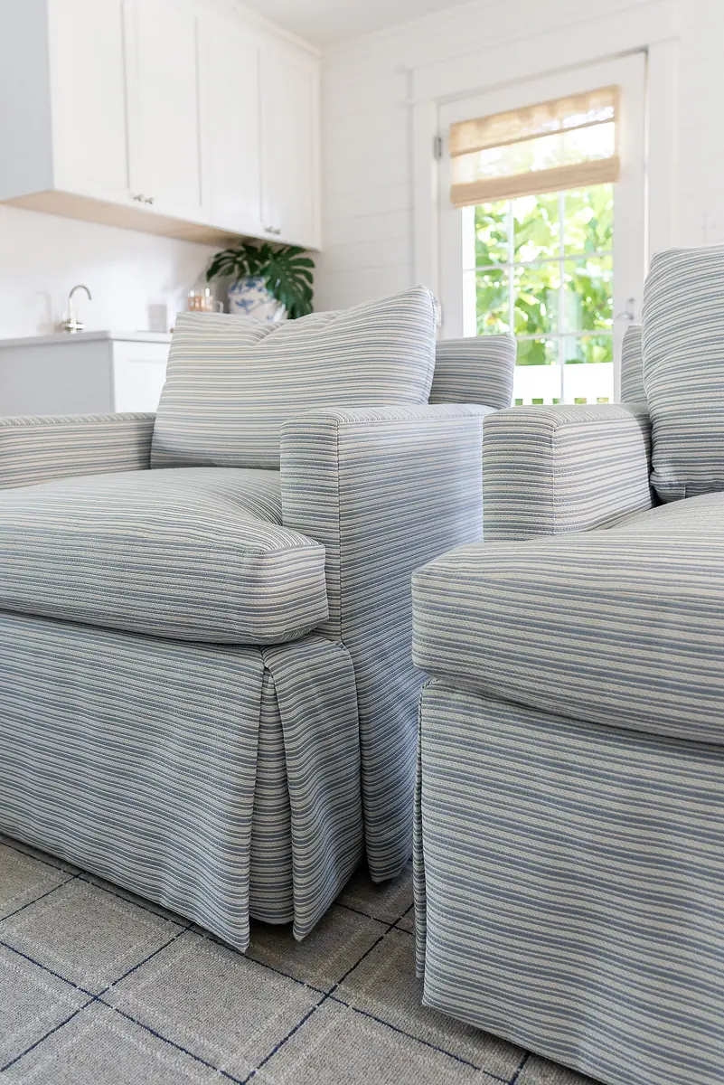 Living room with striped armchairs, woven rug, and a window with light-colored blind.
