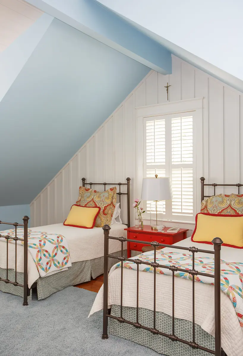 Bedroom with two metal twin beds, colorful quilts, red nightstand, lamp, blue walls, and white paneling