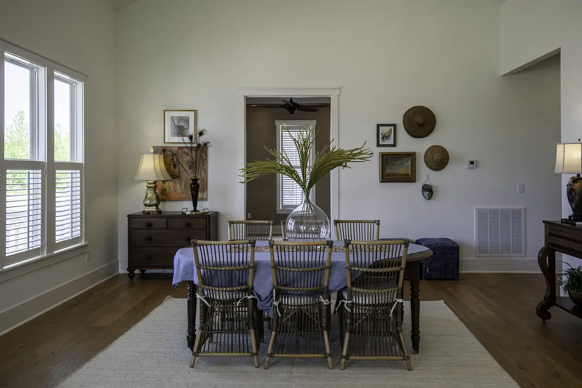 Dining room with wooden table, rattan chairs, vase of greenery, lamps, and framed artworks.