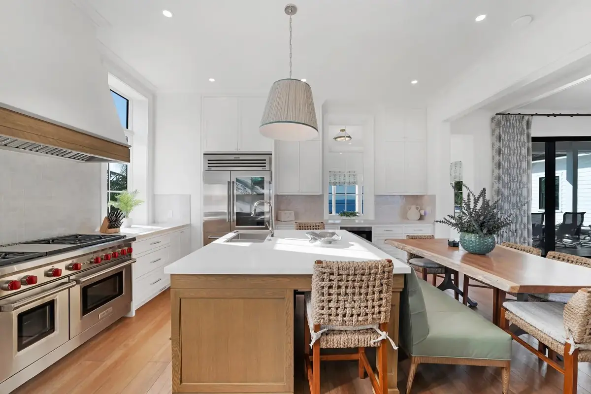 Kitchen with island, stainless steel range, dining table, and green bench seating with natural light from windows.
