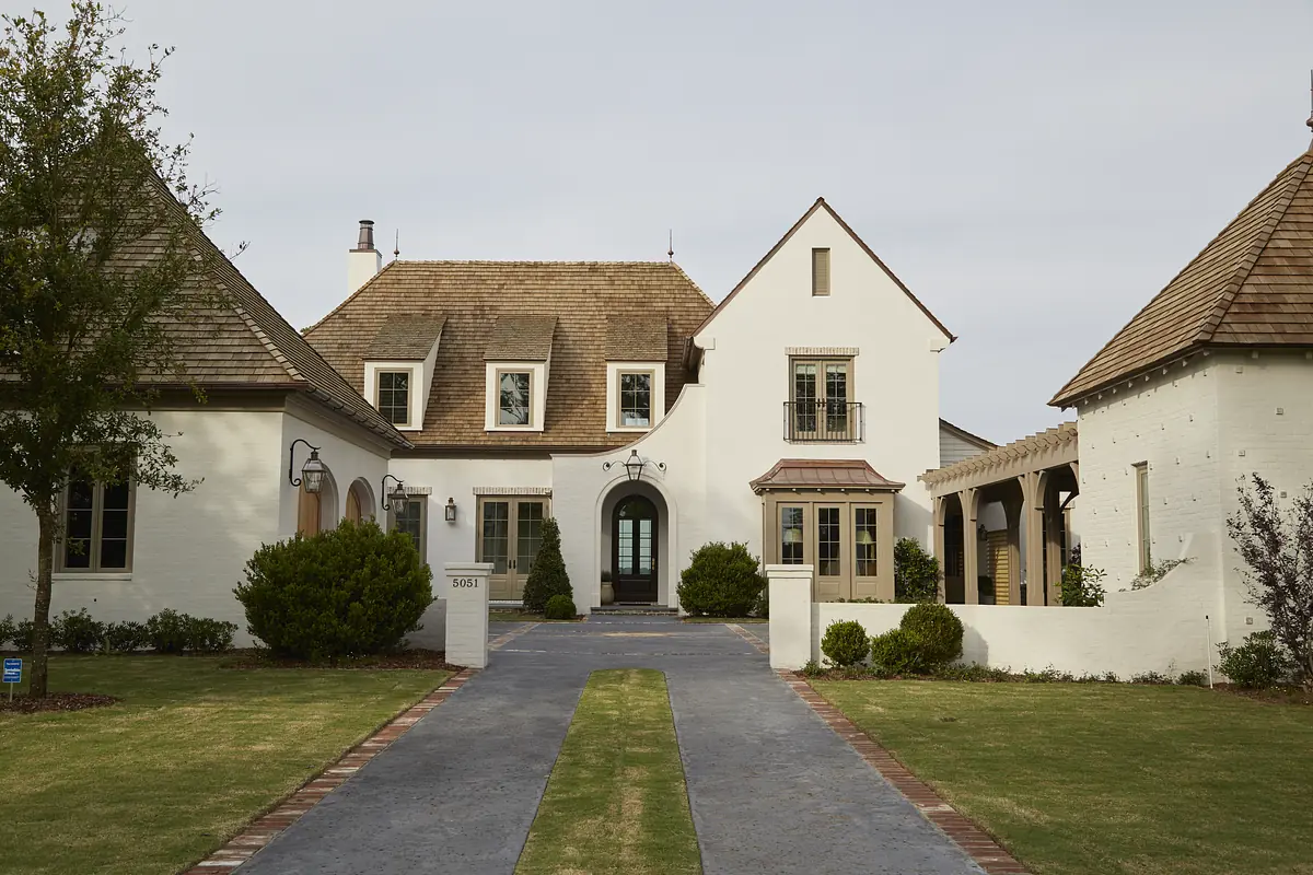 Front exterior view of a house with brick walkway, white walls, shingled roof, and landscaped grass.