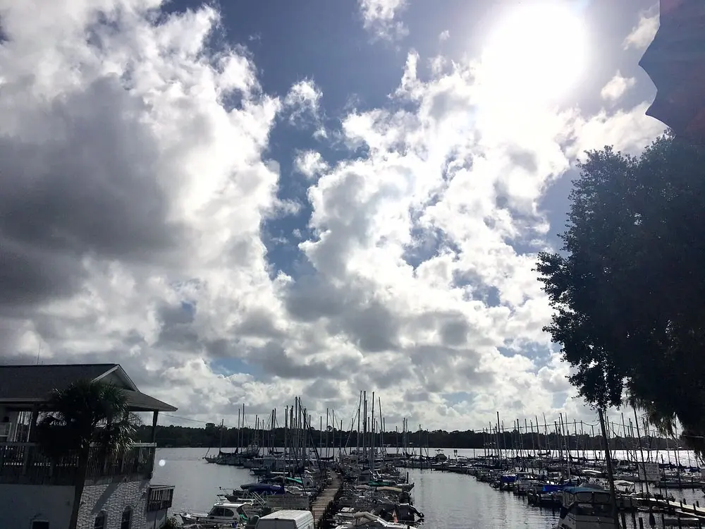 Outdoor waterfront scene with marina, boats, partly cloudy sky, and a building with a porch.