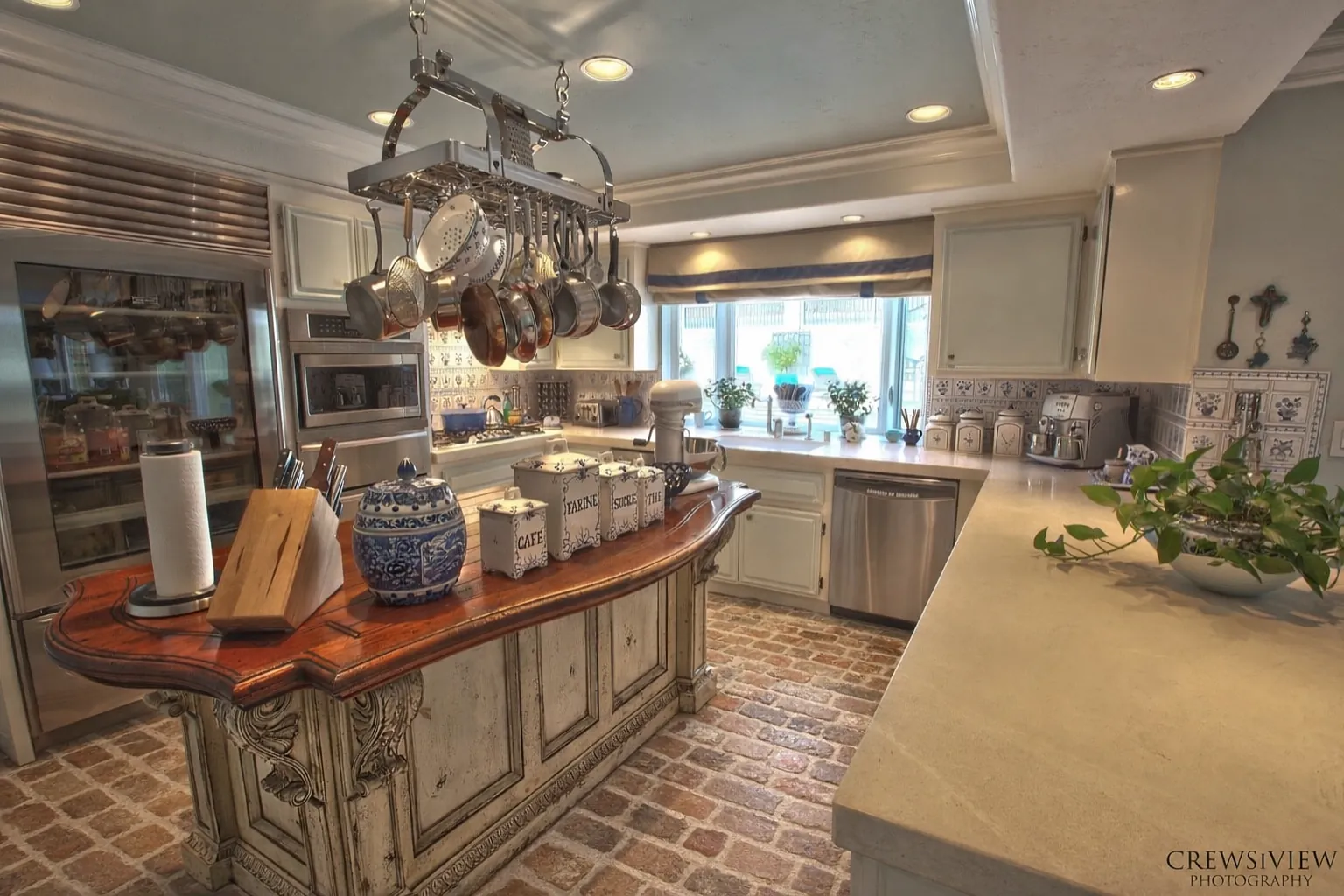 Kitchen with island, stainless steel appliances, pot rack, white cabinets, and decorative tiles.