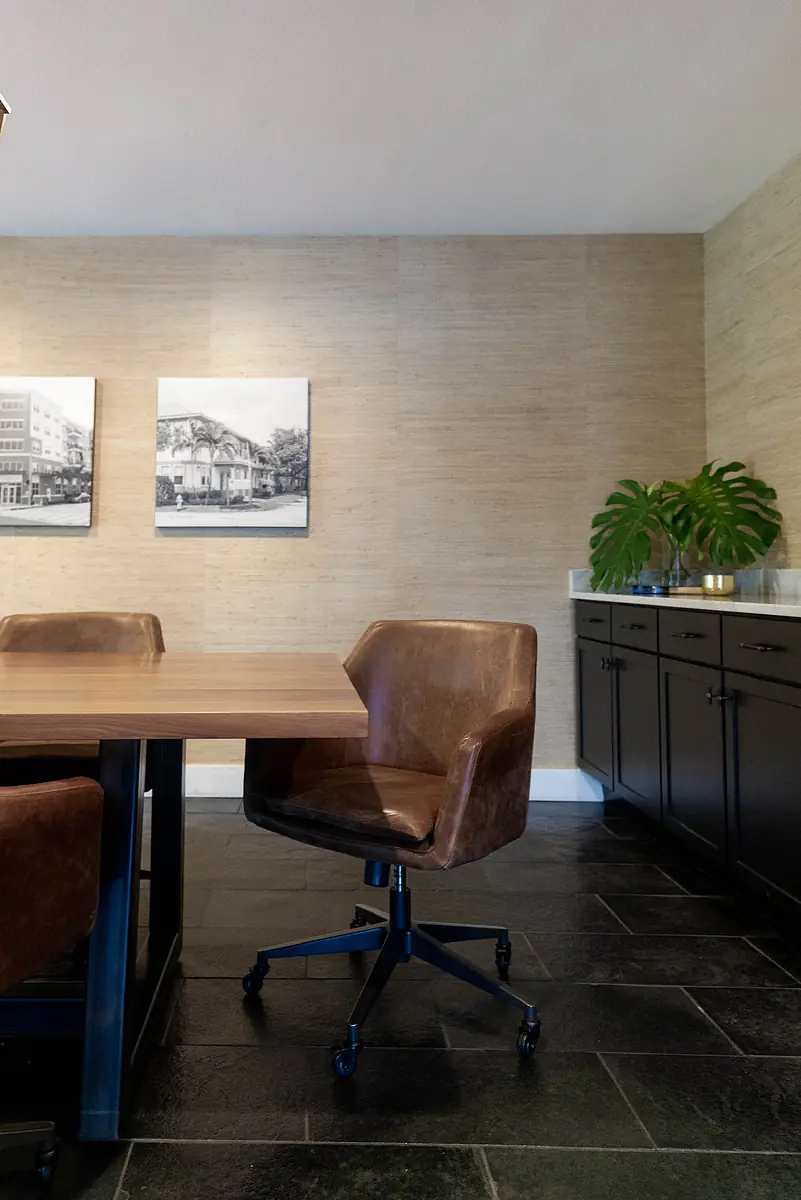 Office with wooden table, brown leather chairs, dark drawers, tiled floor, framed photographs, and a green plant