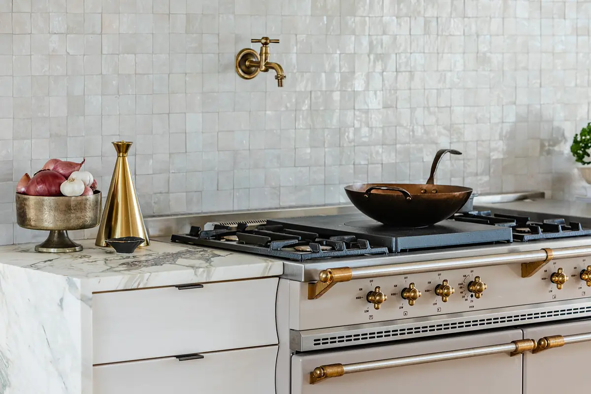 Kitchen with brass faucet, gas stove, white cabinetry, marble countertop, and decorative items.