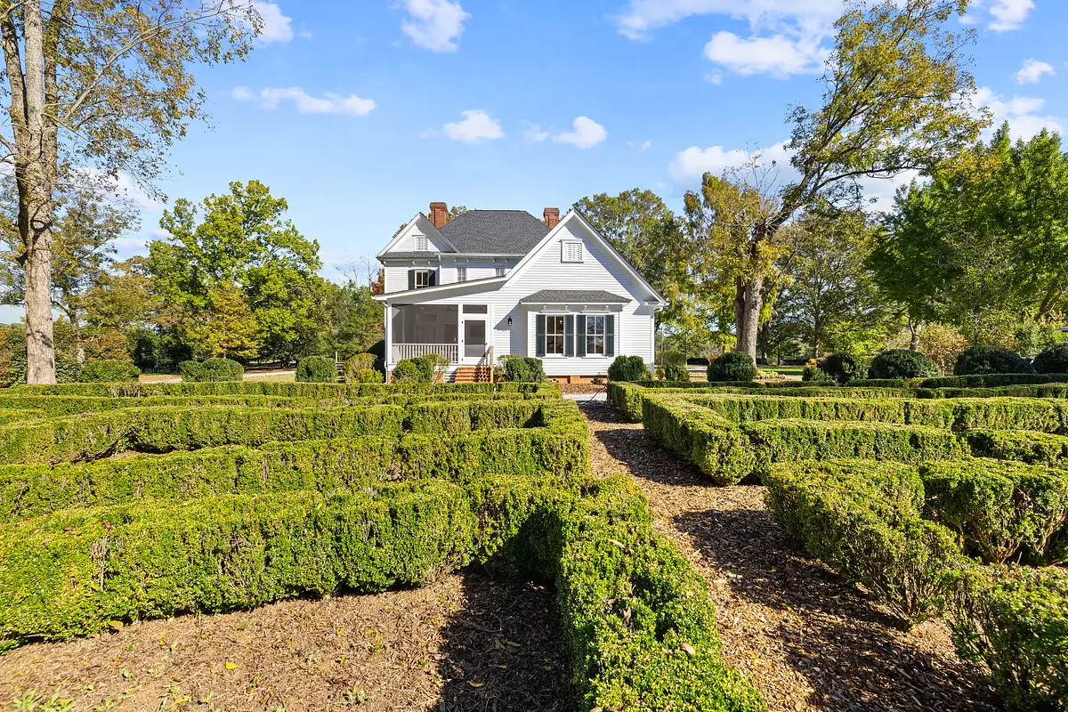 Exterior view of a white house with geometric hedges and gravel pathways.