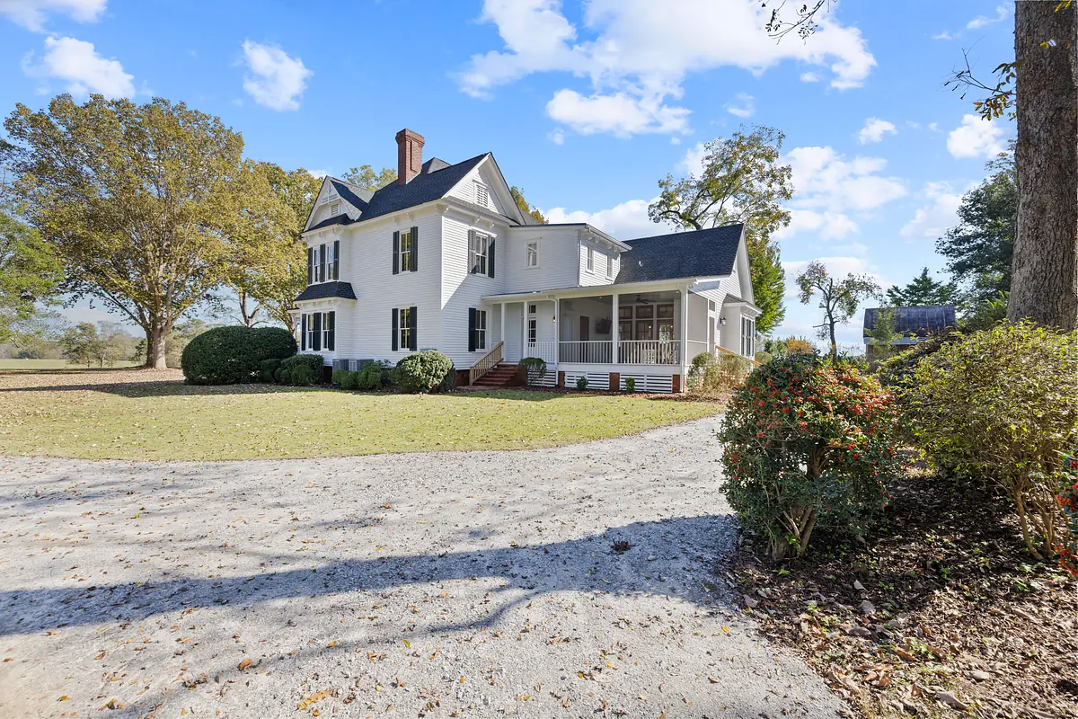 Exterior front of a two-story white house with black roof, porch, and surrounding landscaping.