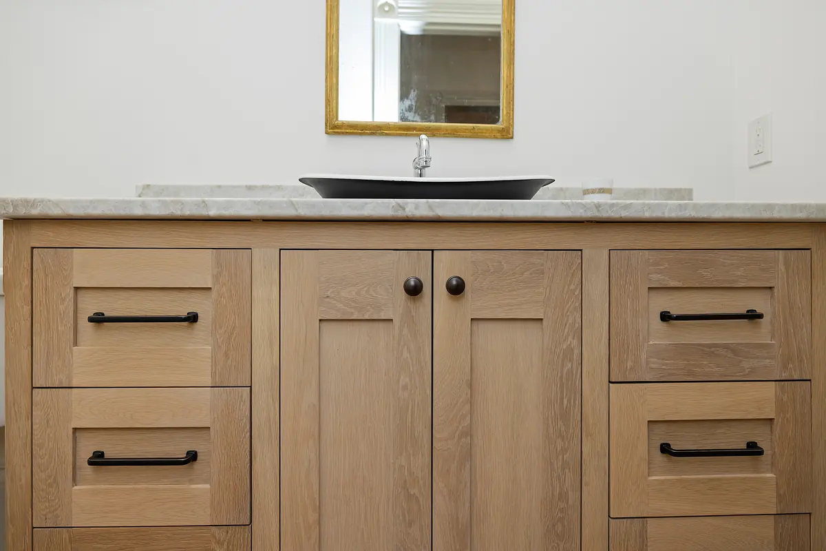 Bathroom with wooden vanity, marble countertop, black vessel sink, and wall-mounted mirror.