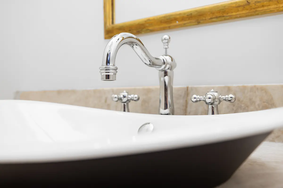 Bathroom with white vessel sink, chrome faucet, beige countertop, and gold-framed mirror.