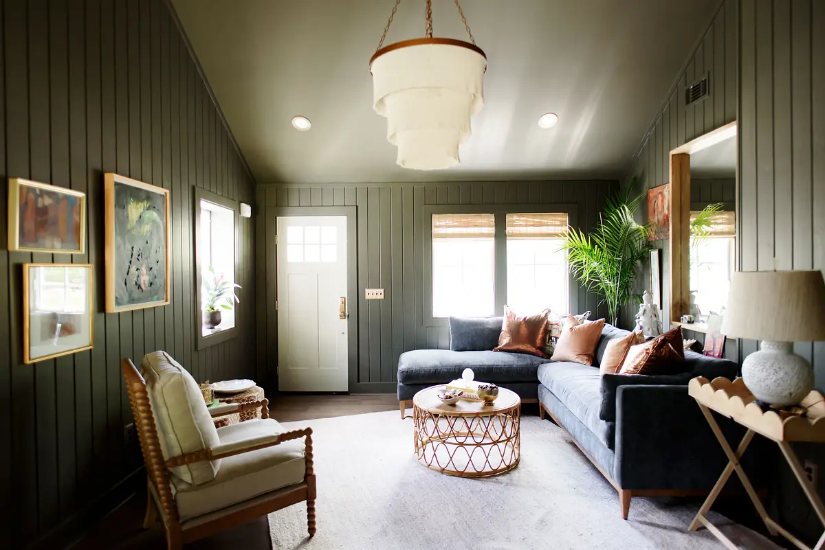Living room with dark sectional sofa, round coffee table, accent chair, wood paneling, artwork, and plant.