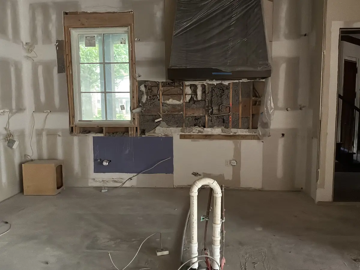Under-construction kitchen space with exposed walls, window, plumbing, and electrical preparations.