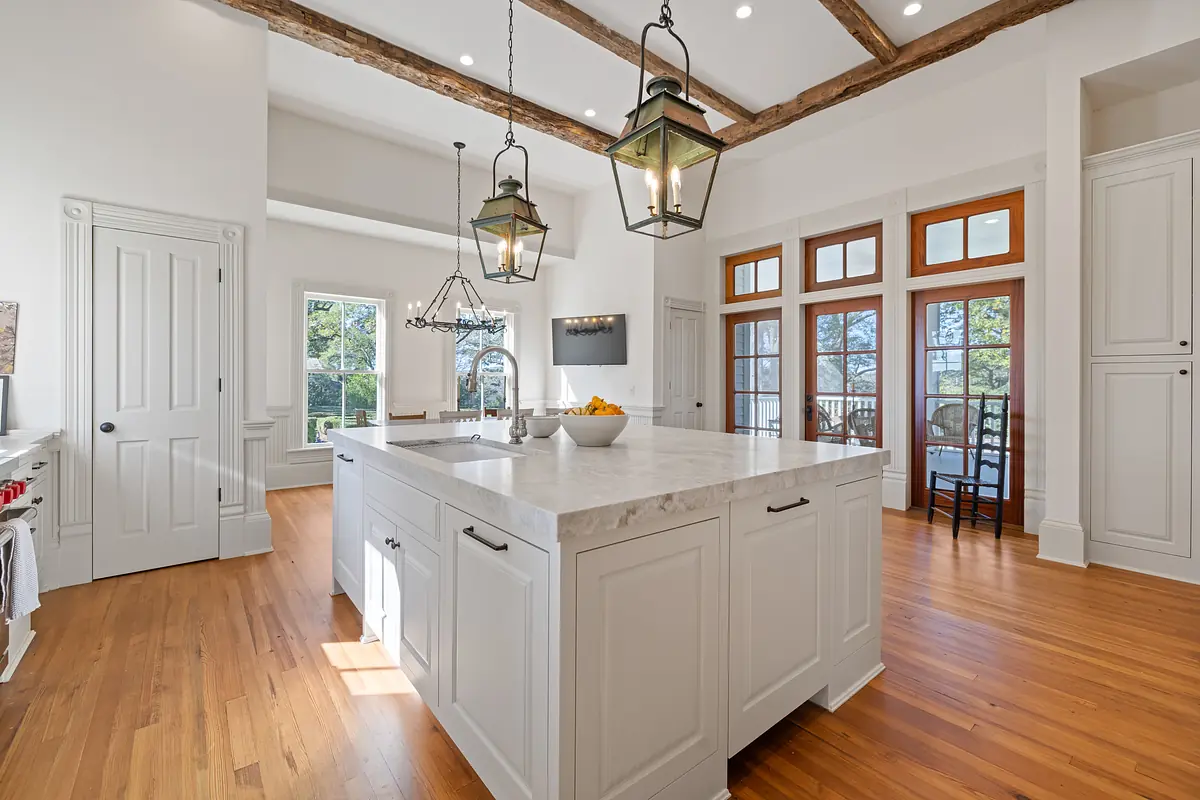 Kitchen with large marble island, white cabinetry, hardwood floor, and lantern-style lighting fixtures.