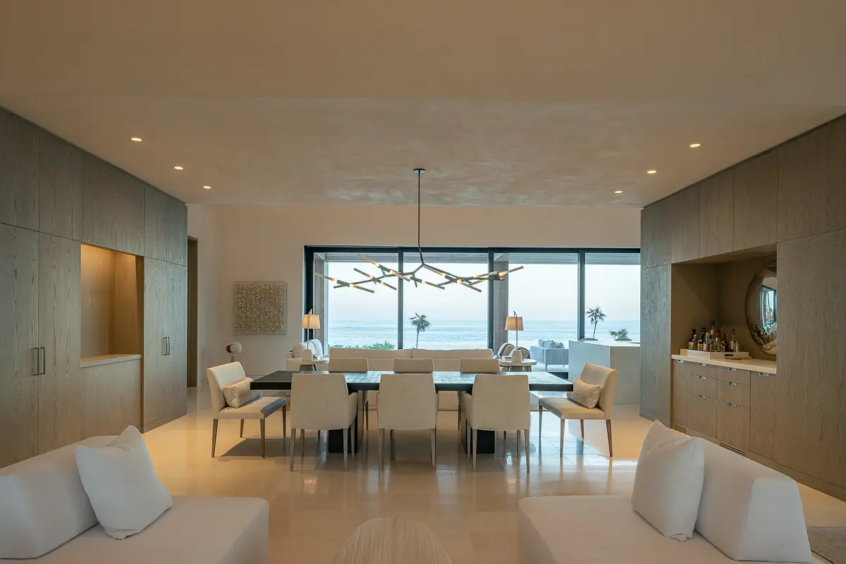 Dining room with rectangular table, white chairs, sideboard, large windows, and ocean views.