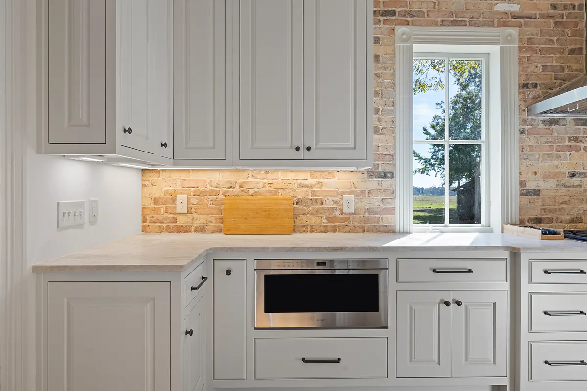 Kitchen with white cabinets, stone countertop, built-in microwave, and large window.