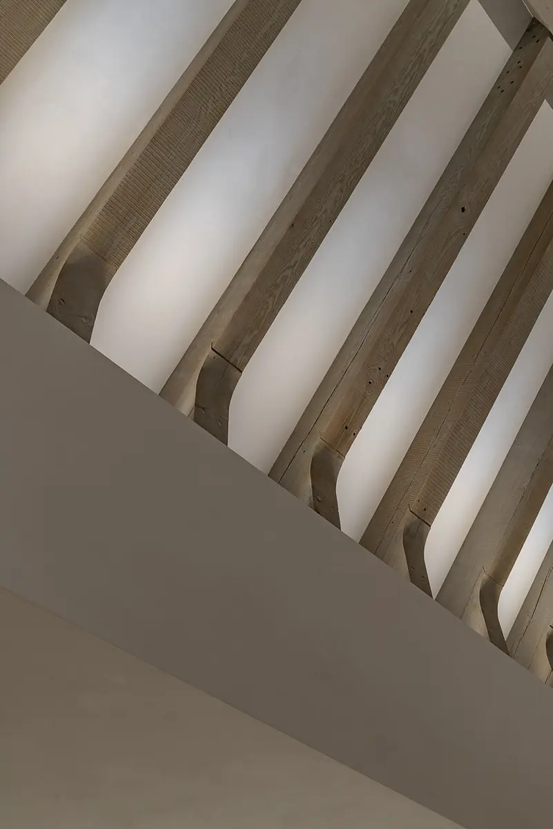 Ceiling view with exposed wooden beams in geometric pattern and smooth white ceiling.