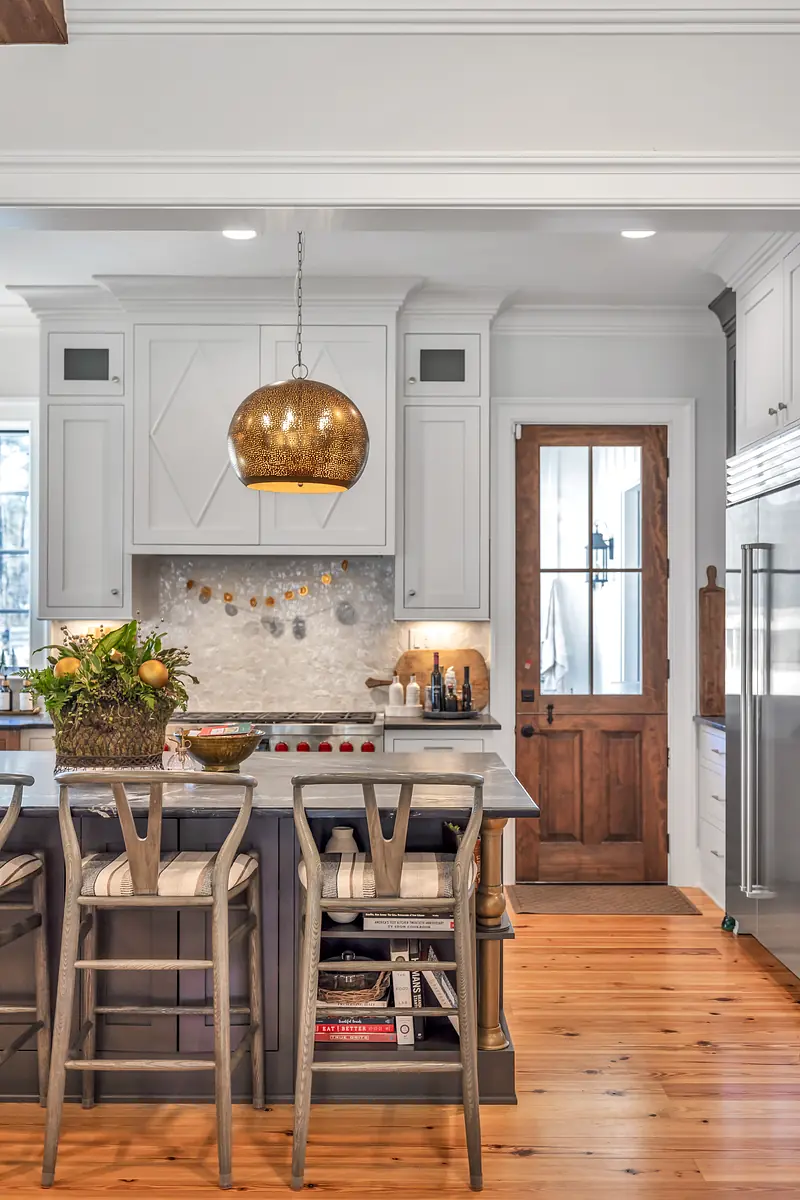 Kitchen with large island, gray cabinetry, white countertop, wooden stools, and door leading outside.