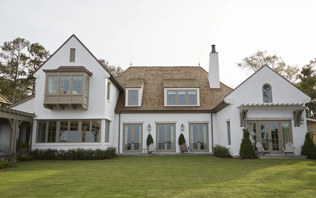 House exterior with sloped roof, multiple windows, deck, lawn, and potted plants.
