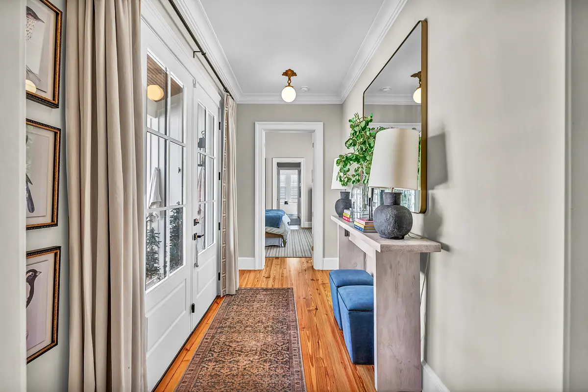 Hallway with a console table, lamp, mirror, framed artwork, and wood flooring.