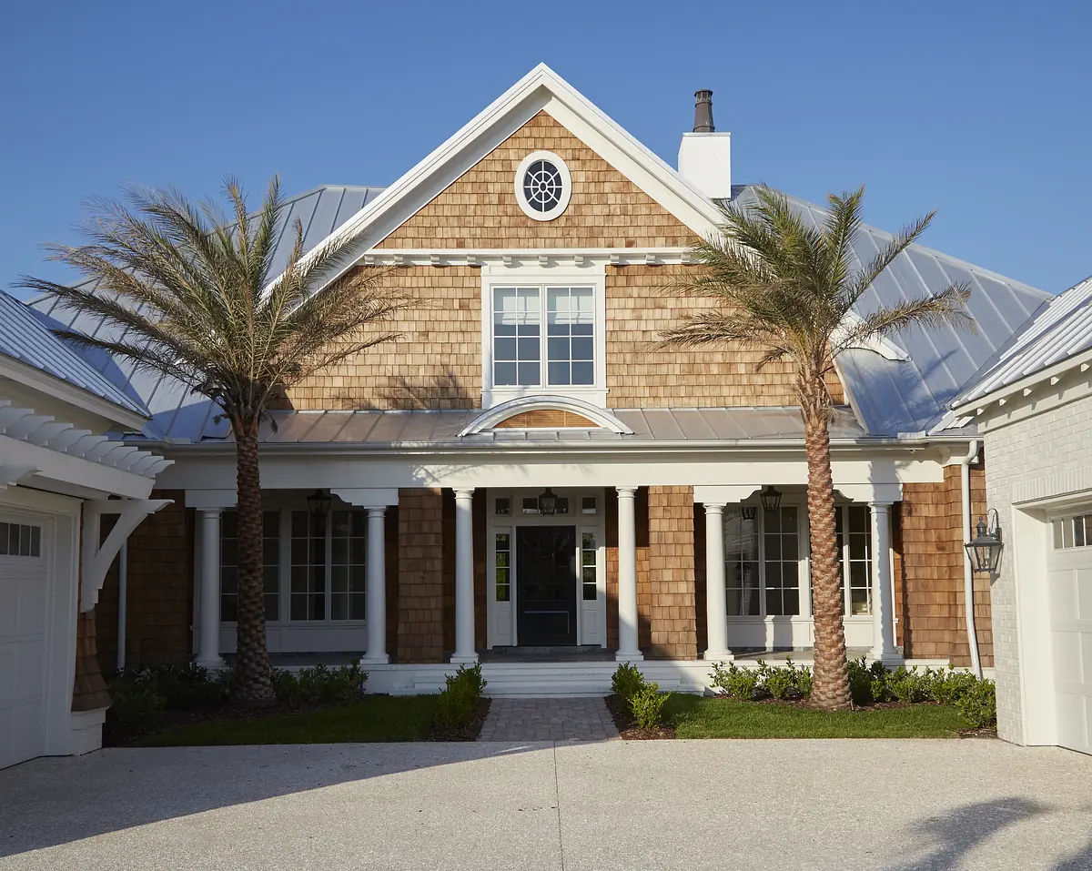 Front exterior of a house with gable roof, wood shingles, central entrance, and palm trees.