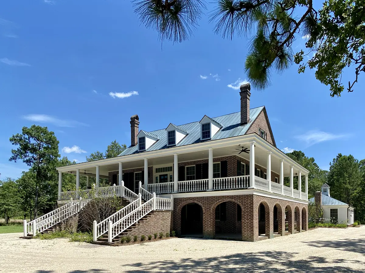 Exterior front of a large brick house with a covered porch, white railing, and wide staircase.