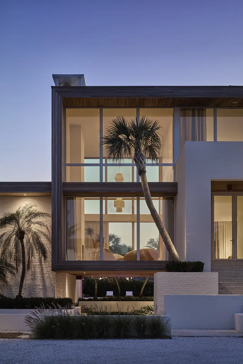 Modern exterior facade with large windows, wood accents, palm trees, and landscaped entrance.