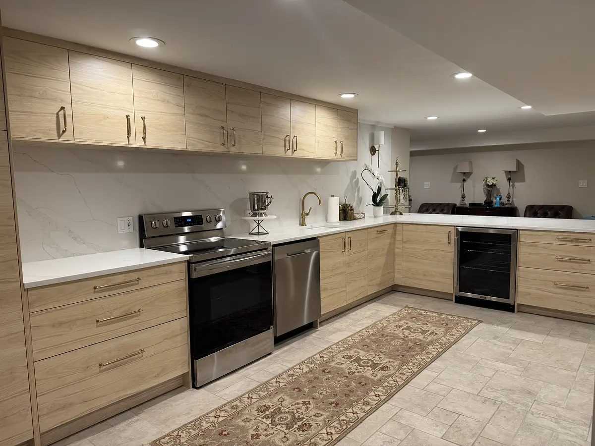 Kitchen with light wood cabinetry, stainless steel appliances, white countertop, and decorative area rug.