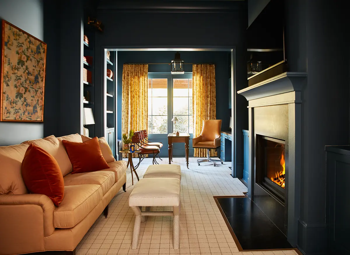 Living room with beige sofa, orange cushions, white ottoman, blue rug, built-in shelves, yellow curtains, and fireplace.