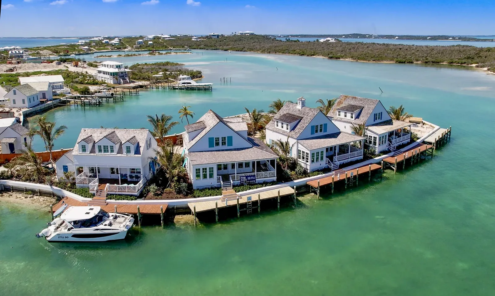 Waterfront view of houses along a boardwalk with palm trees and a boat in the turquoise water.