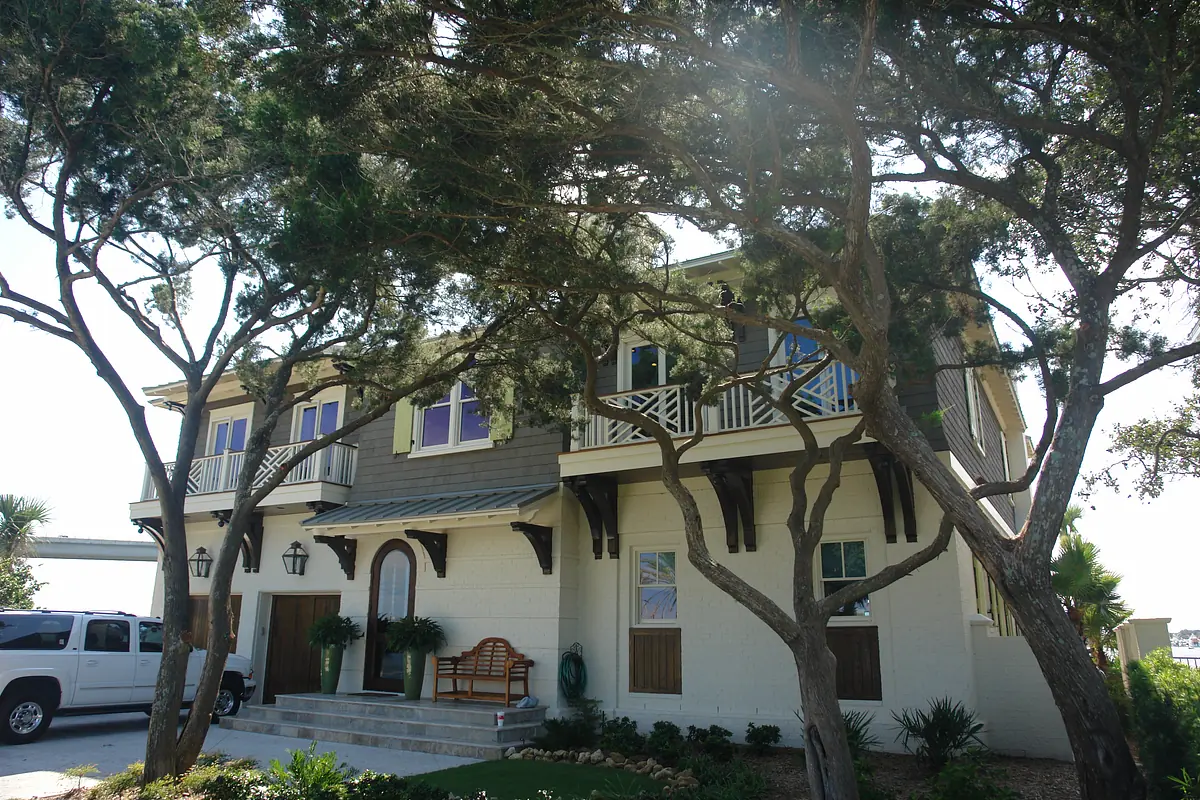 Two-story house exterior with a central entryway, windows, trees, and a pathway.