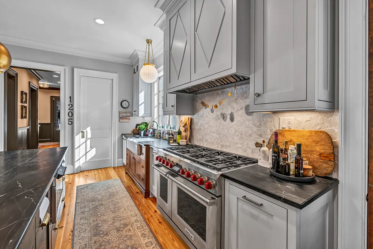 Kitchen with gray cabinets, gas stove, stone countertop, wooden island, and decorative backsplash.