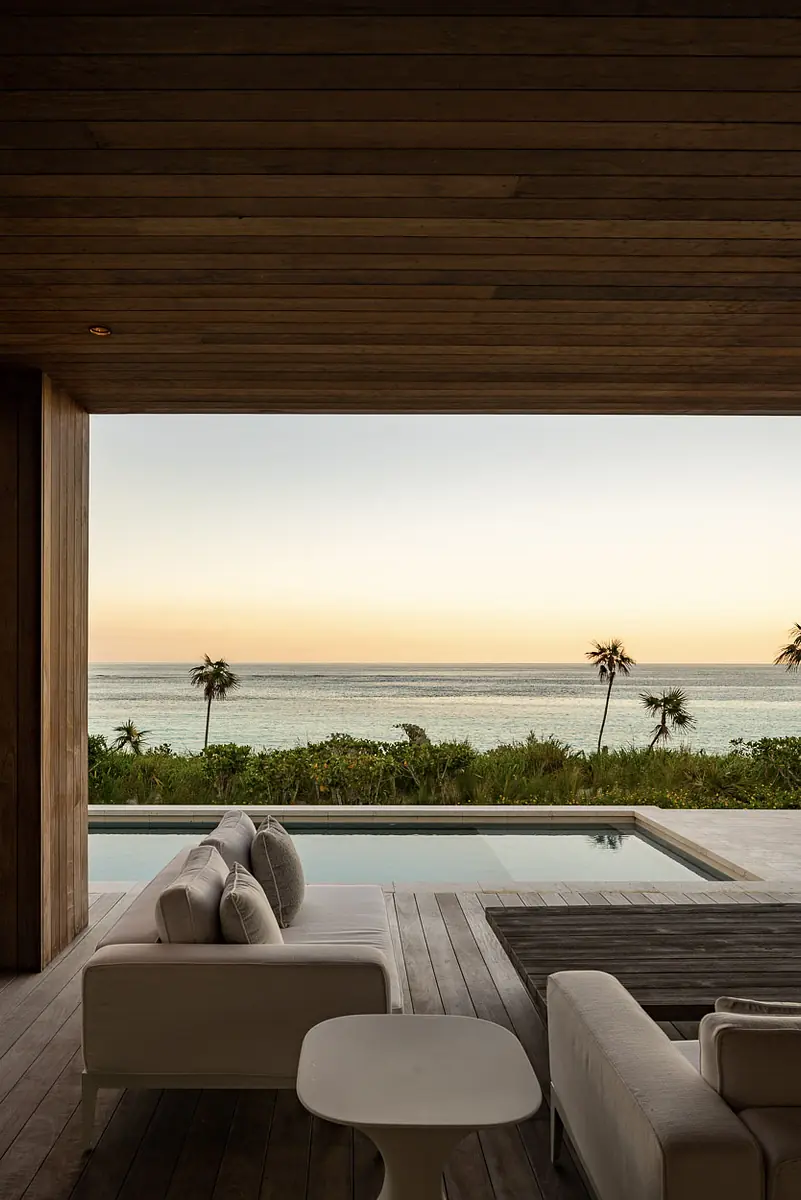 Outdoor deck with white sofas, table, and ocean view with palm trees.