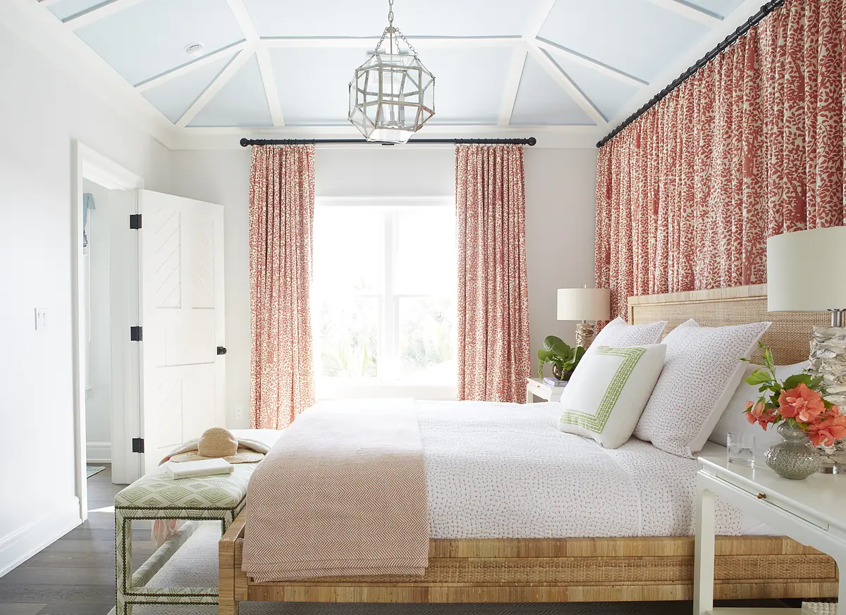 Bedroom with patterned duvet, bench, curtains, light fixture, lamps, and coffered ceiling.