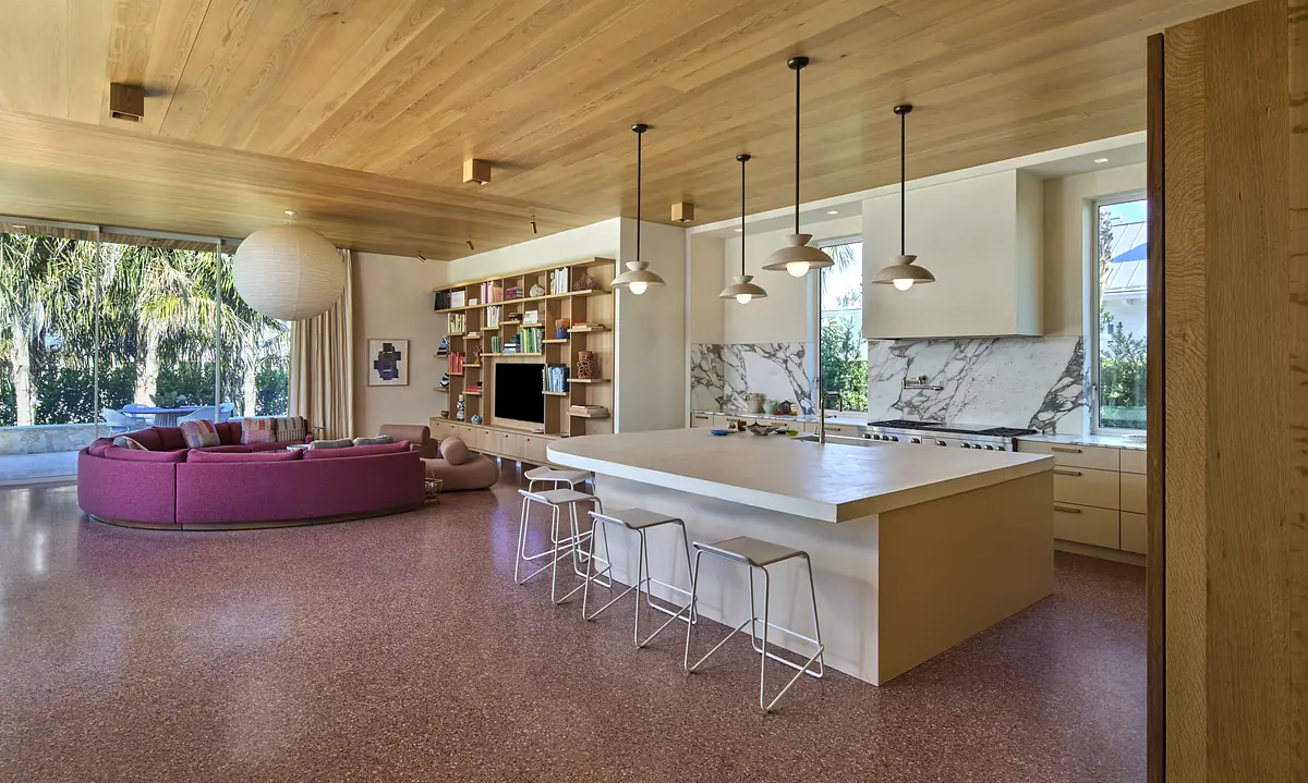 Kitchen with island seating, marble countertops, wall bookshelf, and large window plus purple sofa seating area.