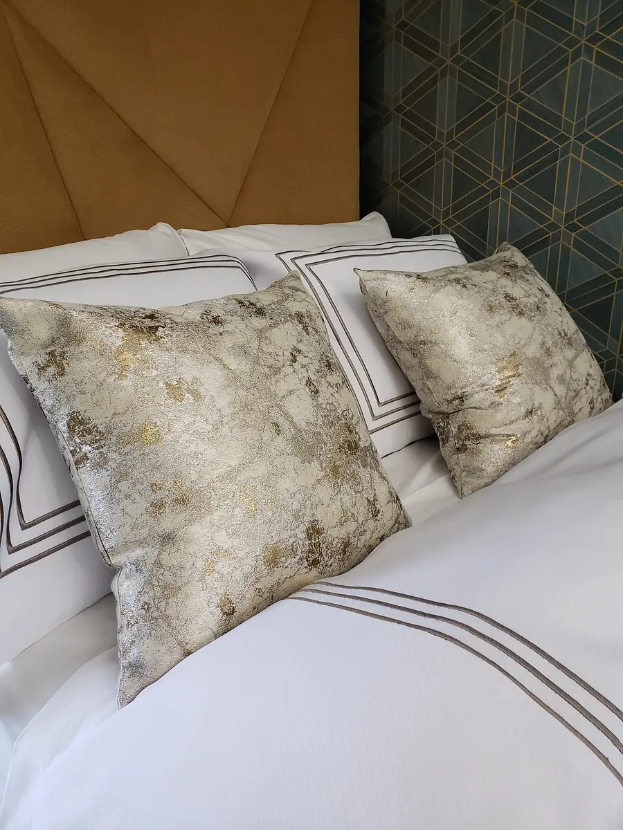 Bedroom with brown headboard, white bedding, gold and gray decorative pillows, and geometric patterned wall.