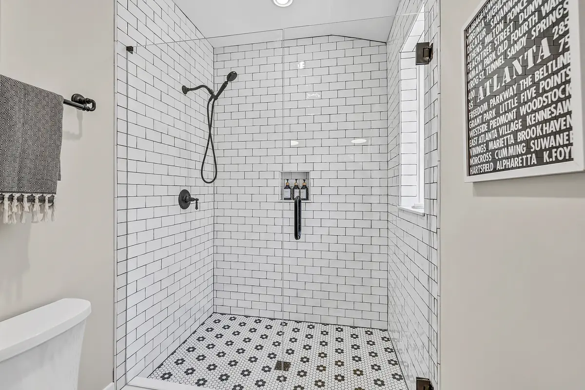 Bathroom with glass shower, white tiles, black floor tiles, towel bar, and graphic wall art.