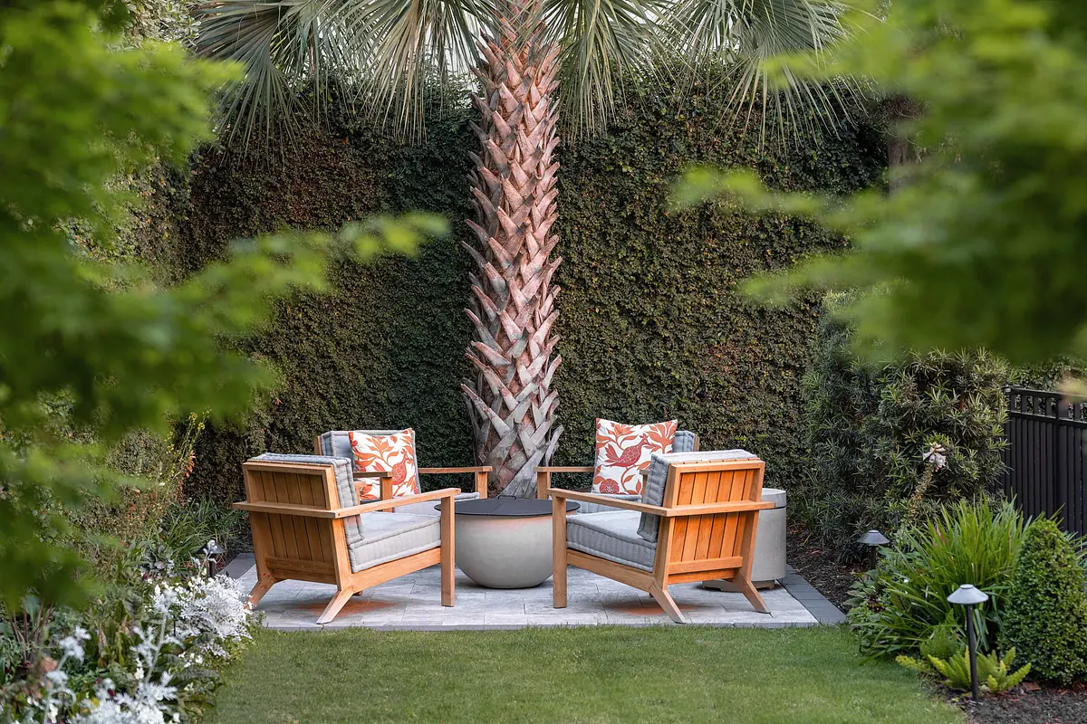 Garden space with wooden armchairs, palm tree, and surrounding greenery.
