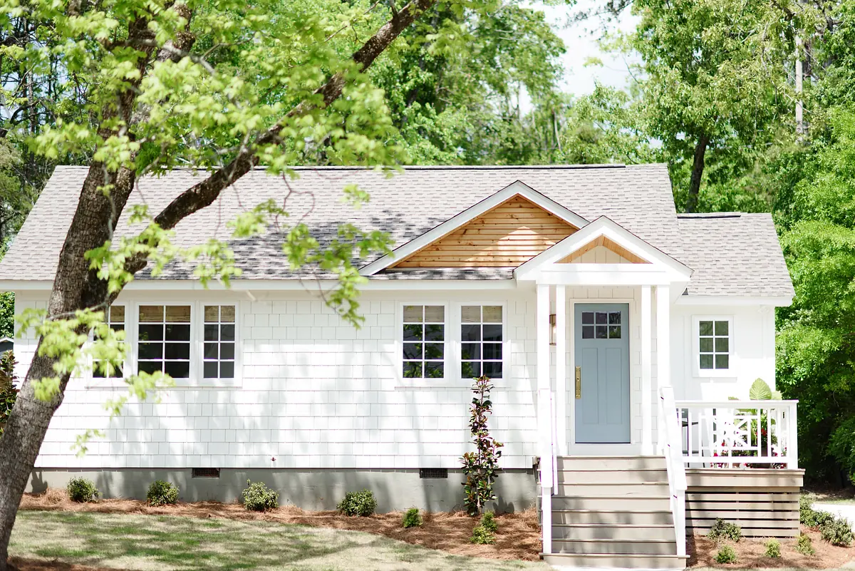 Front exterior of a house with gray door, white siding, five windows, and wooden roof accents.