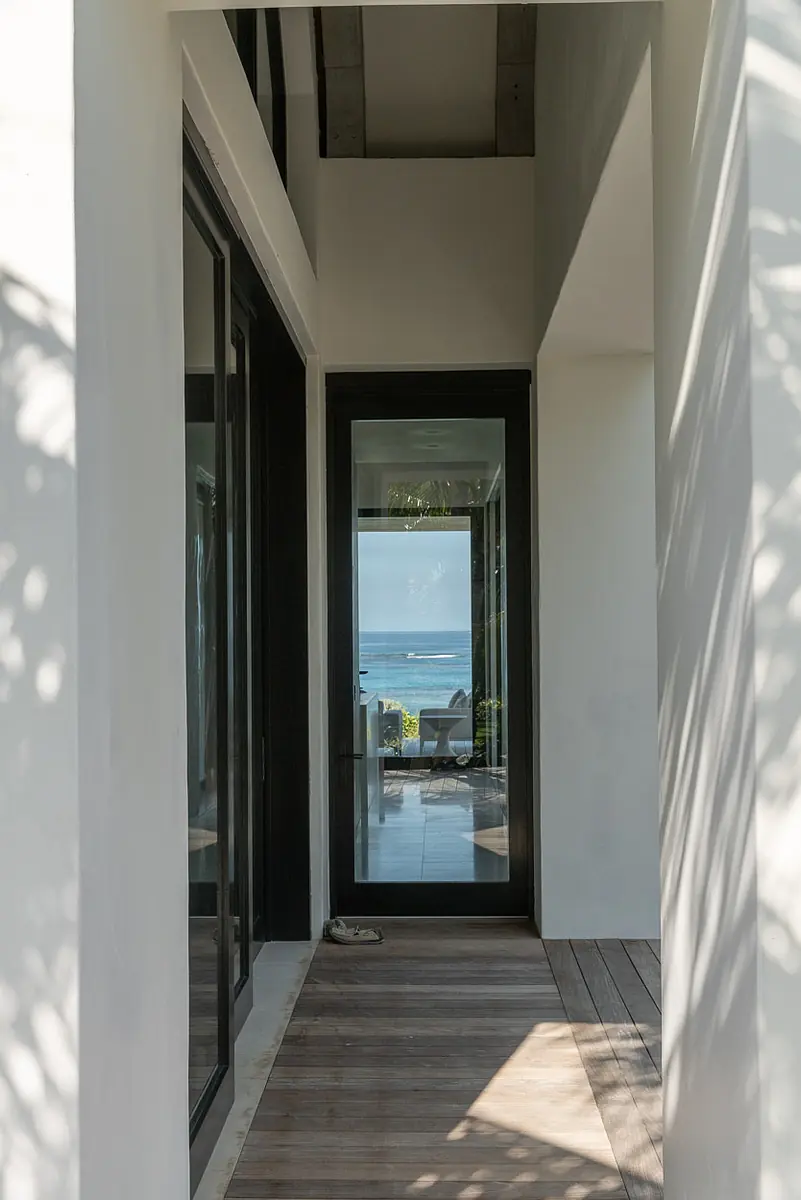 Hallway with large glass doors, ocean view, white walls, wood beams, and wooden plank flooring