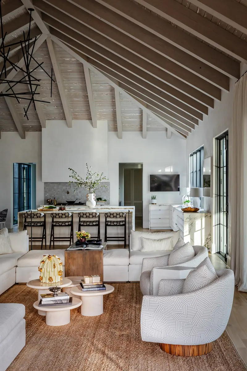 Living room with sectional sofa, round tables, area rug, exposed beams, bar area, and large windows