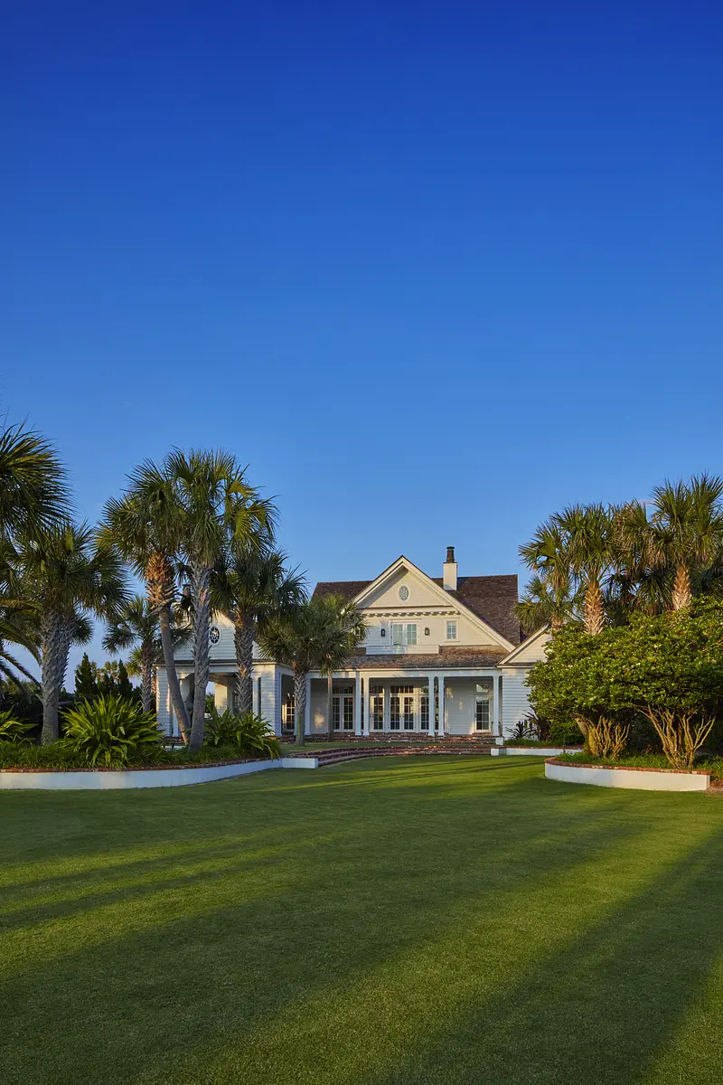 Front exterior view of a house with light blue facade, large windows, and landscaped yard with palm trees.