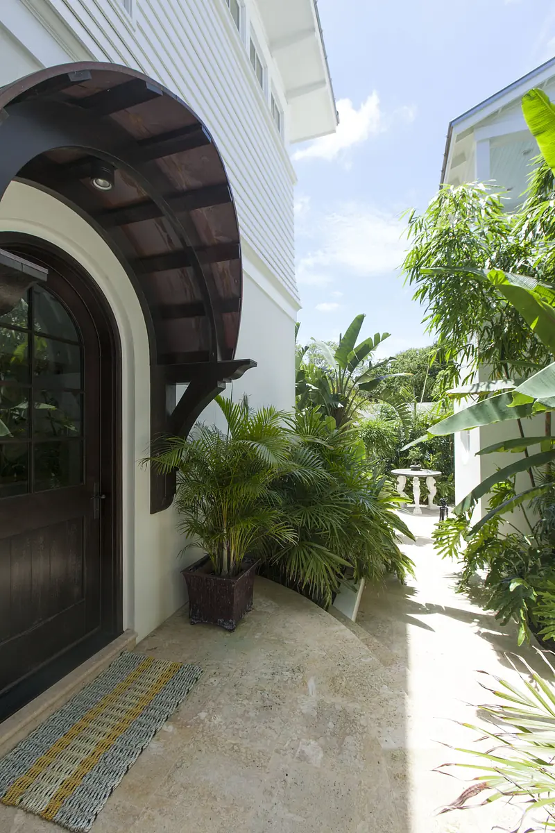 Exterior front with a curved wooden awning, black door, stone pathway, and lush greenery.