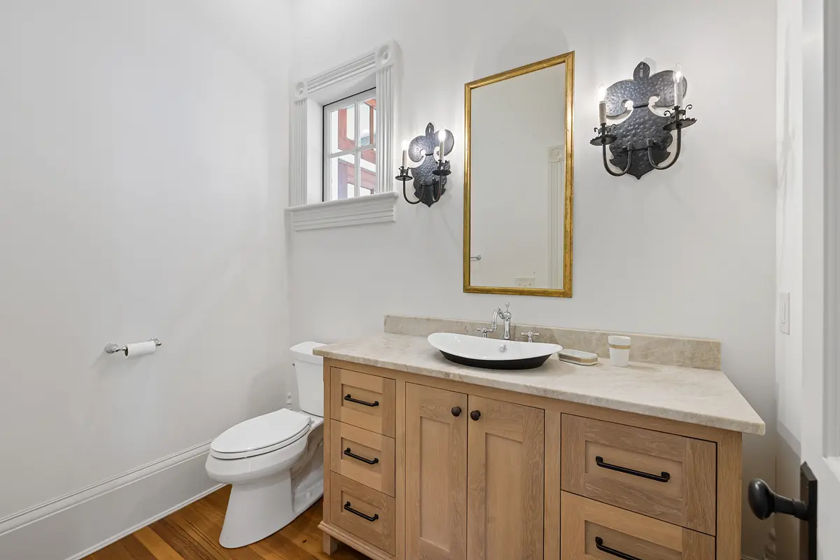 Bathroom with wooden vanity, sink, toilet, wall-mounted mirror, and sconces.
