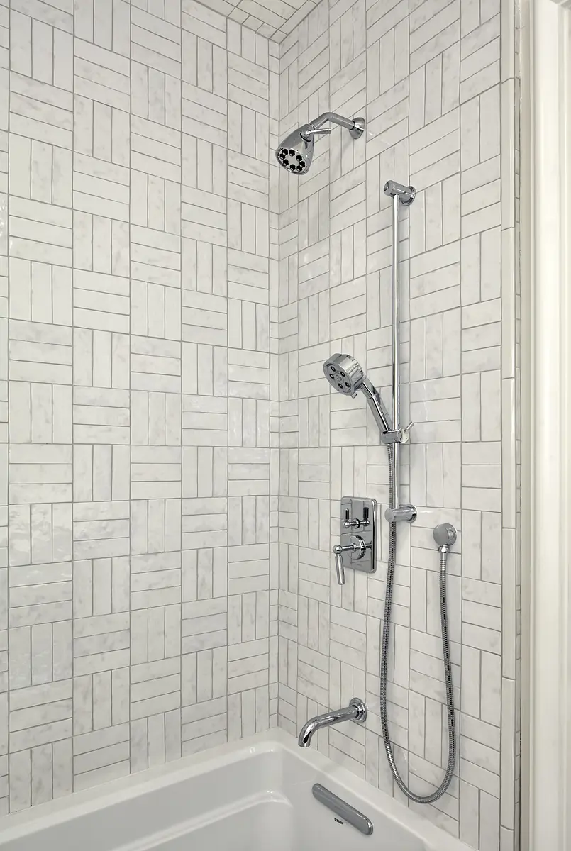 Bathroom with white bathtub, chrome faucet, and light gray tile wall