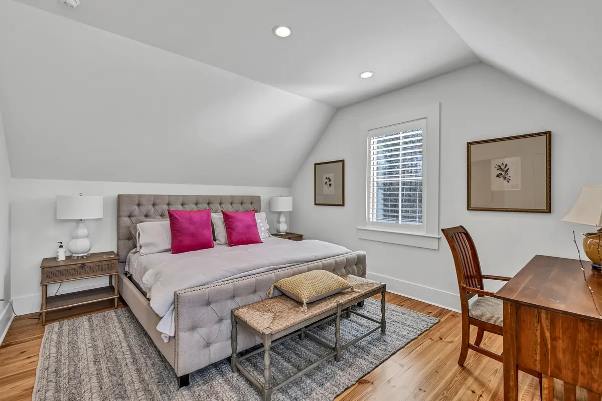 Bedroom with tufted bed, pink pillows, nightstands, desk, and slanted ceiling with natural light.