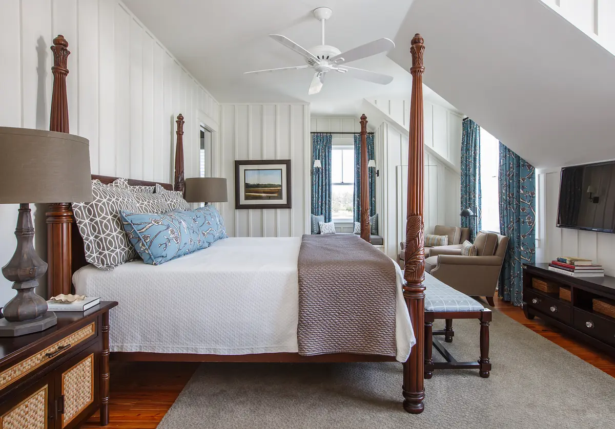Bedroom with four-poster bed, nightstands, rug, curtains, and seating area with armchair and ottoman.
