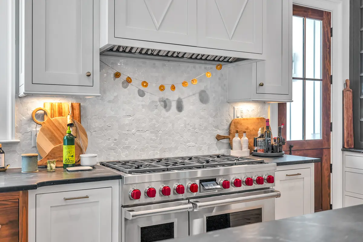 Kitchen with stainless steel gas range, wooden cutting boards, tiled backsplash, and natural wood cabinetry.